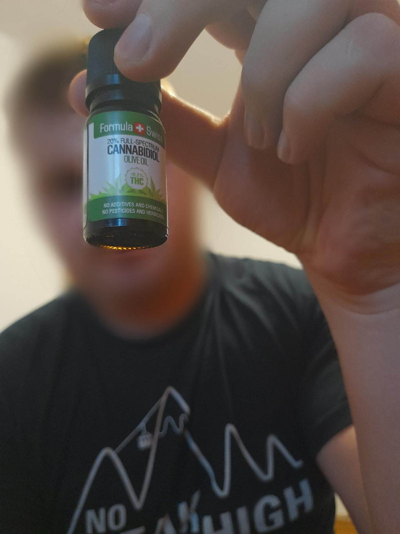 A hand holding up a 10 ml bottle of Formula Swiss CBD oil in olive oil